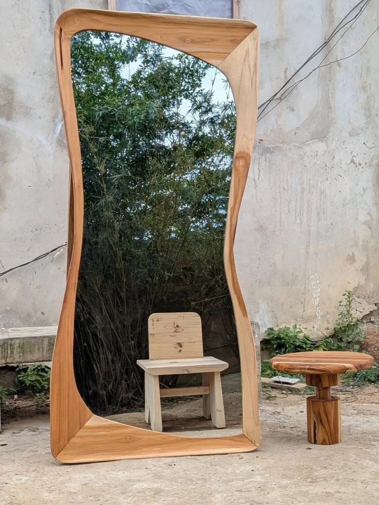 Oversized sculpted solid teak wave-edge full-length mirror in outdoor courtyard
