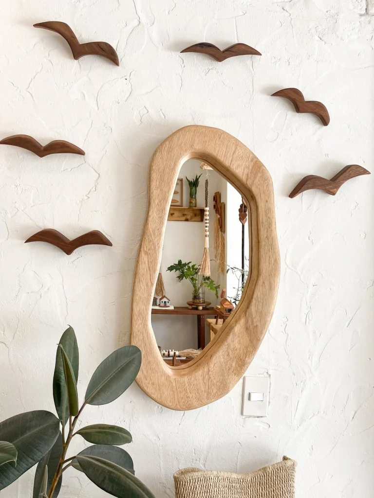 Organic asymmetric pale wood frame mirror on white wall with wooden bird sculptures