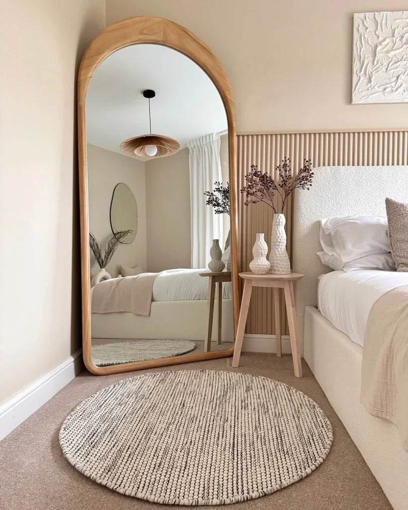 Light oak arched full-length wood frame mirror leaning in neutral bedroom